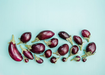 Eggplants of different sizes on a wooden background with mint color. Top view, flat lay.
