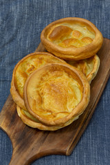 Yorkshire pudding, homemade, stacked on a wooden chopping board with a blue tea towel underneath