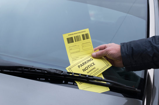 Man got a parking charge notice on windshield. Parking infaction notice, male hand,grey windshield