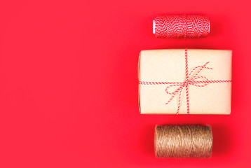 Christmas gift in a craft wrapper red and brown rope on a bright red background with copyspace.