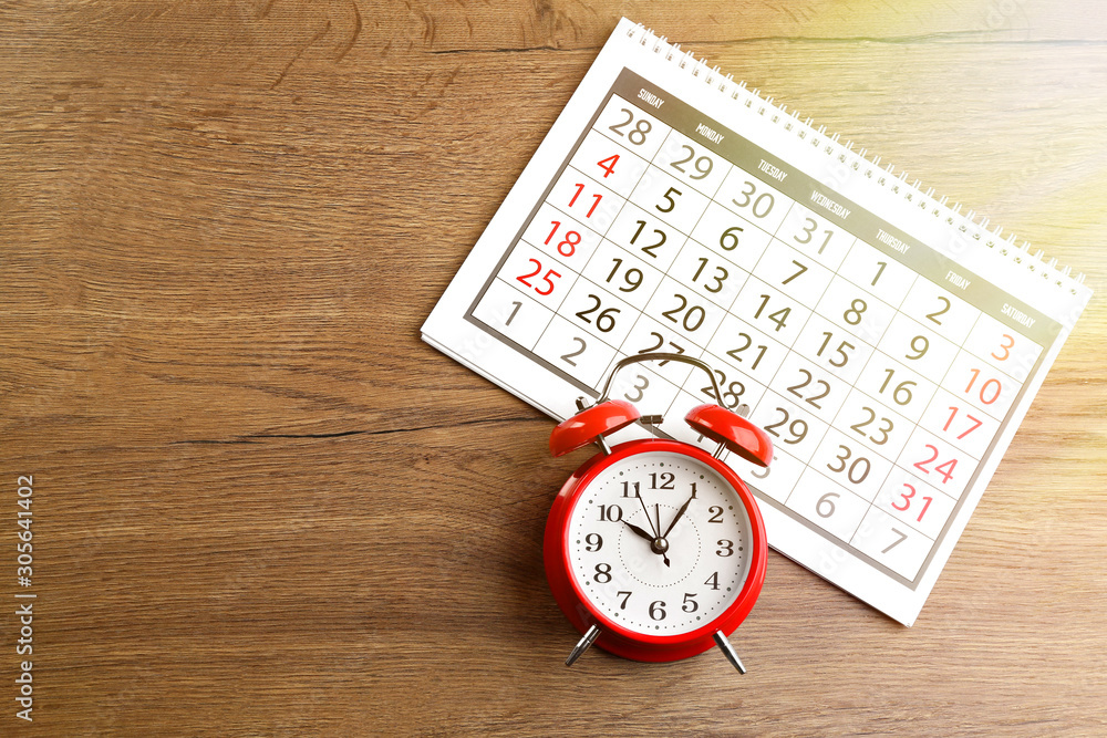 Poster calendar and alarm clock on wooden table, flat lay. space for text