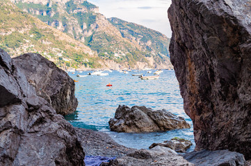 Big boulders lying on the beach, people resting, sunbathing and swimming in Tyrrhenian sea in Positano amazing medieval city on rocky mountains in Campania