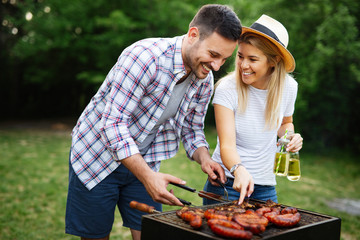 Young couple preparing sausages on a barbecue outdoors - Powered by Adobe