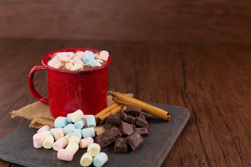 Cup of hot chocolate with marshmallows on wooden board, pieces of pure chocolate and cinnamon - red pewter cup- Guatemalan chocolate