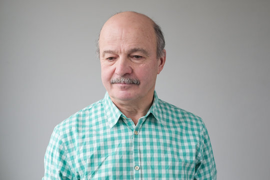 Close Up Studio Shot Of Senior Hispanic Bald Man With Mustache Looking Down Being Upset With News.