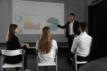 Male business trainer giving lecture in conference room with projection screen