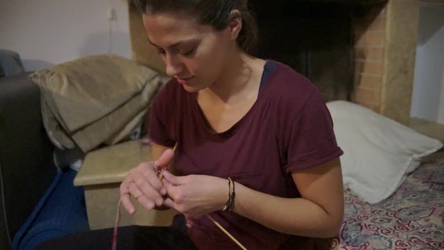 Footage of caucasian brunette woman knitting in front of the fireplace 
