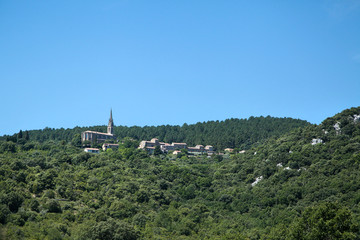 French countryside landscape at sunny summer day. Catholic church (église Saint-Pierre-ès-Liens) among green hills in village of Banne, Ardeche, Rhone-Alpes, southern France