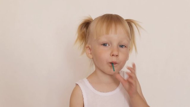 Little caucasian girl 3 years old with pigtails sucks and licks candy on a stick