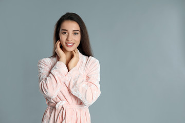 Beautiful young woman in bathrobe on grey background. Space for text