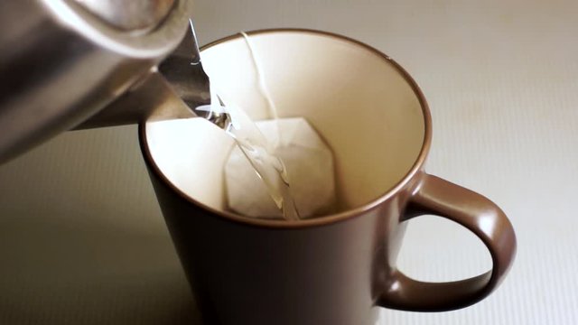 Making hot black tea in bag in a brown cup . Water is poured from a chrome kettle. Top view, close-up