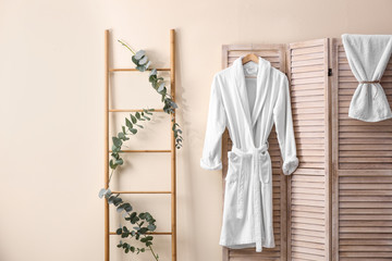 Soft comfortable bathrobe hanging on folding screen in stylish room interior - obrazy, fototapety, plakaty