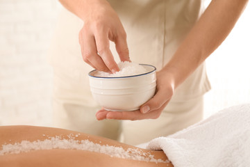 Young woman having body scrubbing procedure with sea salt in spa salon, closeup