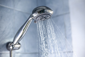 Fototapeta na wymiar Closeup of a silver shower head splashing water in the bathroom, cold shower benefits