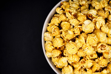 Delicious popcorn with caramel in bowl on black color background