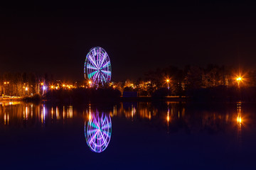 Illuminated observation wheel at night reflected in water