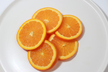 The thin round pieces of orange slices put together on the white dish.
