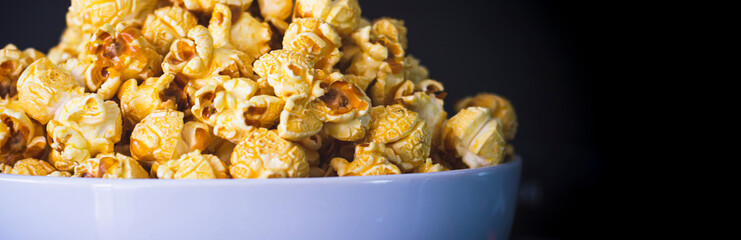Delicious popcorn with caramel in bowl on black color background