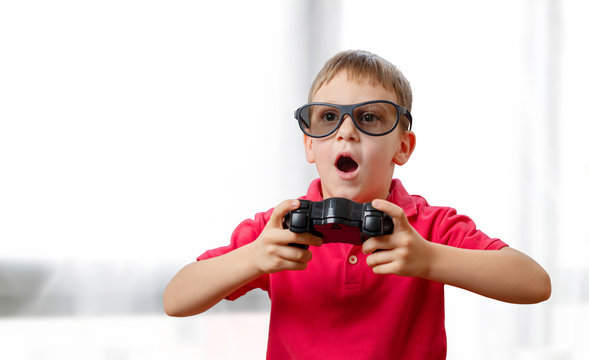 The boy plays games with a joypad and 3d glasses. His mouth slightly open with excitement.