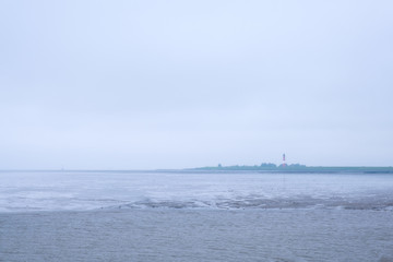 Blick zur Insel Pellworm/Deutschland mit Leuchtturm bei Nebel und Ebbe