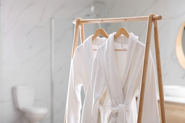 Fresh white bathrobes hanging on rack indoors