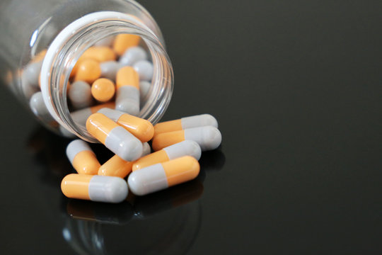 Pills in a bottle, medication in capsules on a dark glass table. Concept of pharmacy, vitamins, background for cold and flu season
