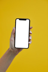 Fototapeta na wymiar Woman hand holding mobile smartphone with white screen on a yellow background.