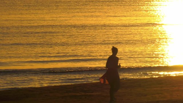 Fit Woman jogging barefoot on sandy beach at dawm, sunlight reflecting on water, slow motion