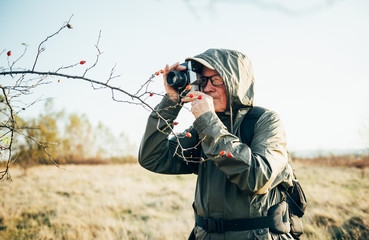 Old man taking photo in nature. Man photographing autumn forest.