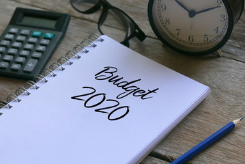 Calculator.glasses,clock,pencil and notebook written with Budget 2020 on wooden background.