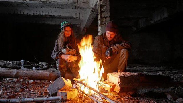 Woman and man travelers sit near a fire in an underground city