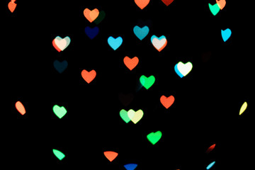 Multicolored hearts bokeh of blue and orange colores on black background. Texture for holidays