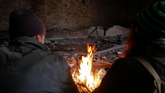 man and a woman are sitting near a fire in an underground shelter