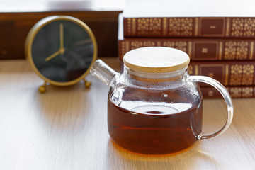 Glass tea pot with black tea on wooden table