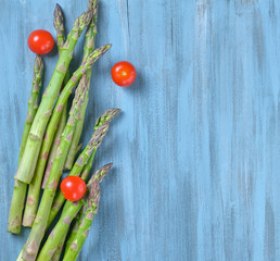 Creative flat lay with Bunch of fresh green Asparagus and fresh red cherry tomatoes on old blue wooden background. Top view on minimal layout made of raw stalks asparagus on wood rustic backdrop.