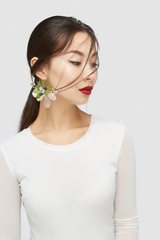 Naklejka premium Medium shot of a young Asian lady in a white blouse and with golden earrings with sparkling crystals and pendants in the form of flower arrangements with gems and golden beads strings. 