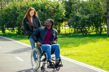 afro american man sitting on wheelchair ,his redhaired ginger girlfriend rolling stroller in autumn...