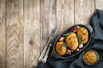 Baked potatoes with herbs, spices, garlic and sauce in a black pan on a rustic background top view free copy space.