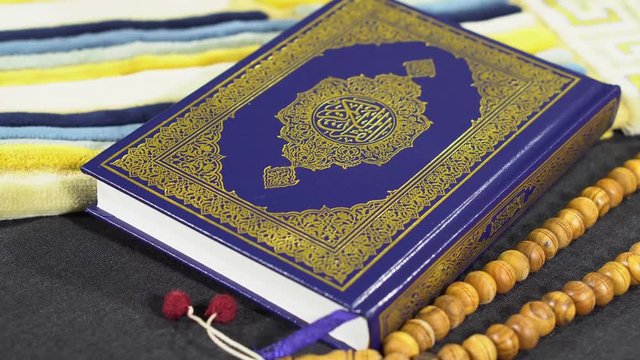Tilt up shot of Muslims Holy Book Quran Kareem AL Quran Majid with wooden Tasbeeh Paternoster and Prayer Rug Janamaz on black background - 4K
