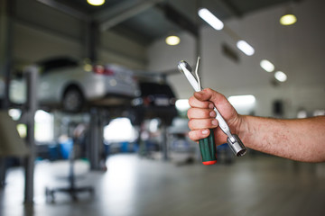 A mechanic in overalls with tools in his hands stands with his arms crossed on his chest. Work in the service station in the background.