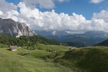 Landscapes of mountain and grassland with small wooden lodge in Seceda, with clouds and blue sky, in Dolomites mountain range in summer