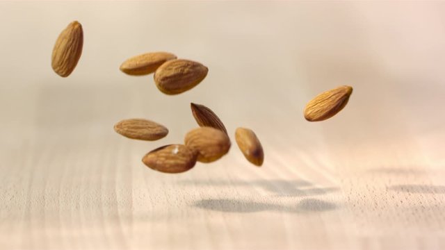 Nicely Illuminated Shot Of Almonds Falling On Wooden Surface
