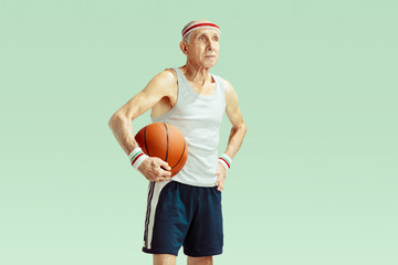 Senior man wearing sportwear playing basketball isolated on green background. Caucasian man in...