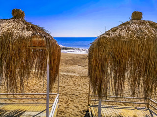 Two gazebos with thatched roofs on the beach against the blue ocean in a sunny summer day. Tropical...