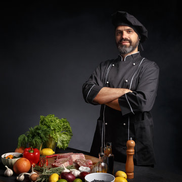 Male chef in black uniform posing near a table with groceries.