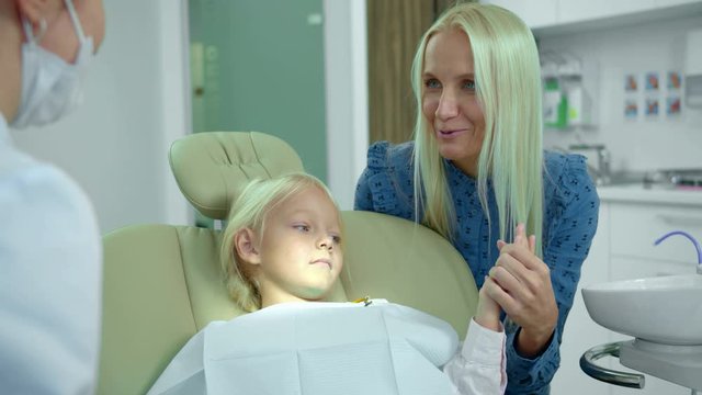 Mother sits with her daughter and talks to dentist