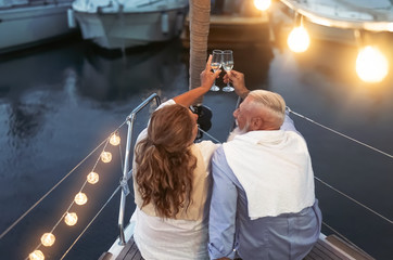 Senior couple toasting champagne on sailboat vacation - Happy mature people having fun celebrating wedding anniversary on boat trip - Love relationship and travel lifestyle concept