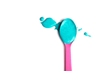 A pink spoon with turquoise mint paint lies on a white background. Isolated.