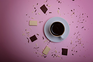 A cup of espresso coffee, pieces and crumbs of dark and white chocolate on a pink background. Flatlay. View from above.