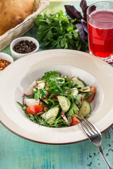 Plate of healthy green garden salad with radish, tomato and cucumber on blue wooden table